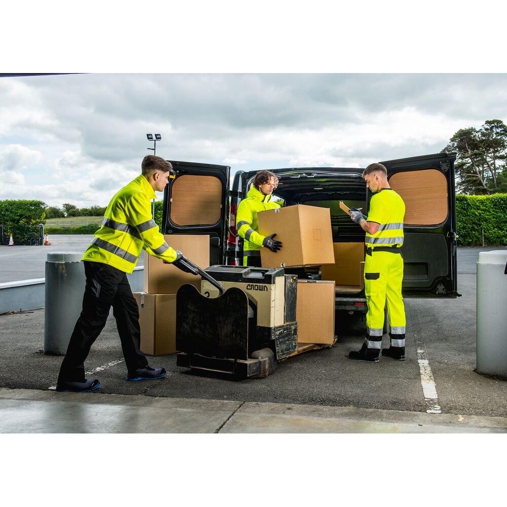 Pracownicy rozładowujący kartony z odzieżą roboczą i środkami ochrony indywidualnej z dostawy do firmy.